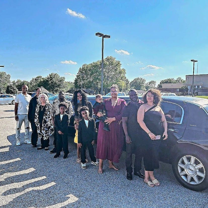 Group of people dressed formally standing beside a black limousine in a sunny parking lot.