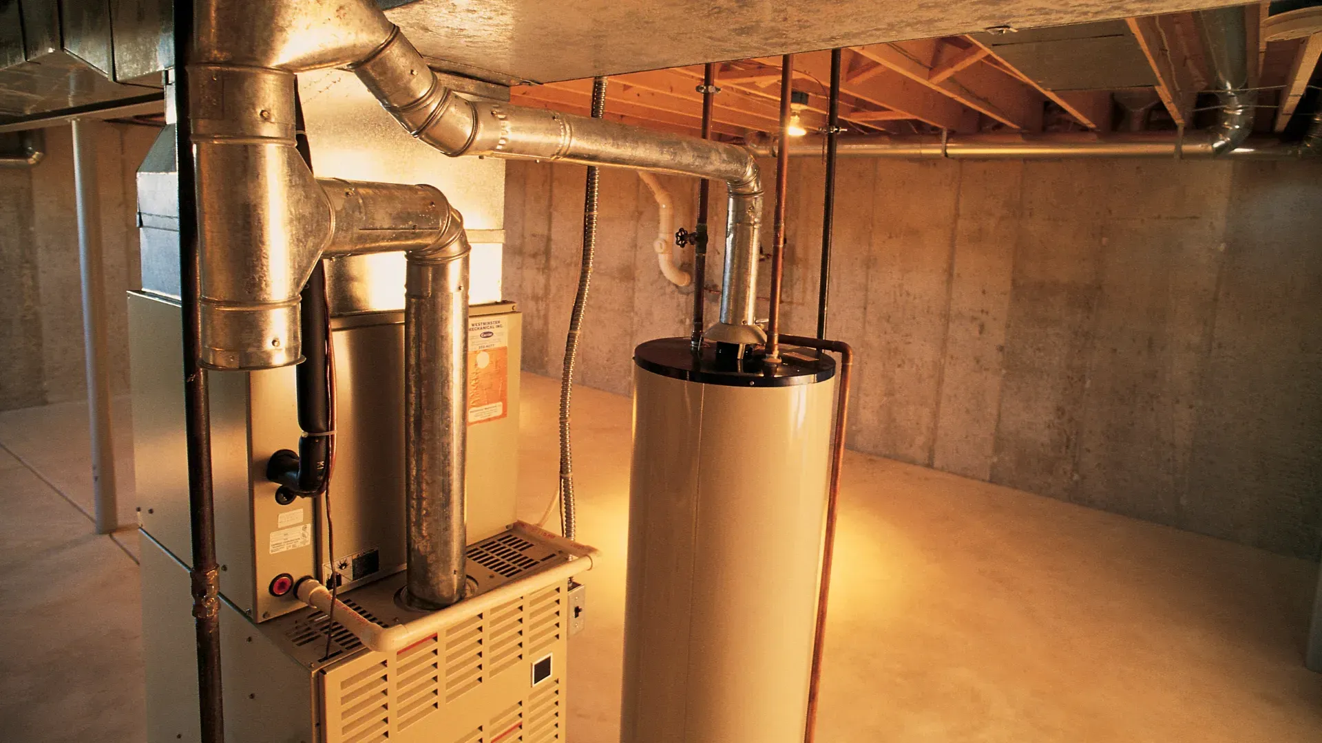 Furnace and water heater in a basement with concrete walls and exposed wooden beams.