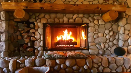 Fireplace with stone surround, burning logs, and wooden mantel.