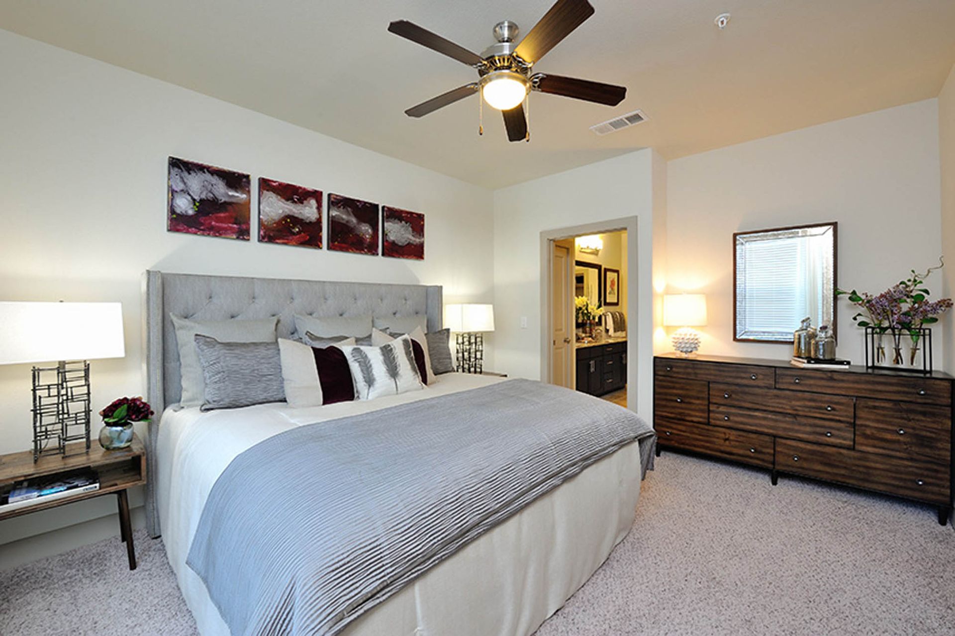 Bedroom in an apartment with a large bed, tufted headboard, two nightstands, dresser, and ceiling fan.