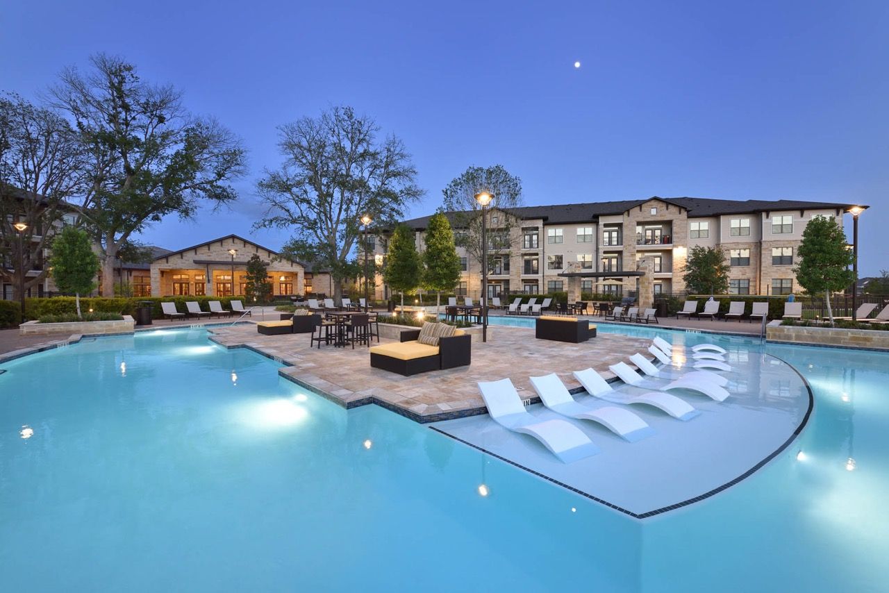 Outdoor community pool with lounge chairs and seating area, with apartment buildings in the background.