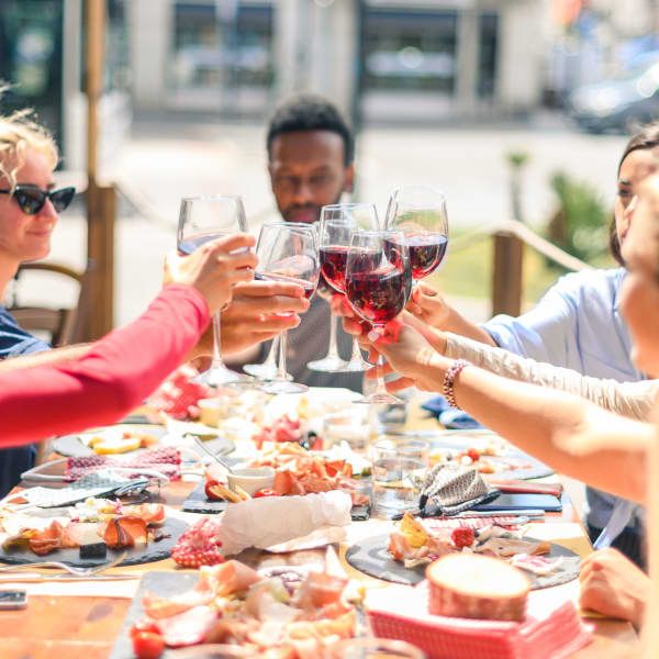 Four people toast with glasses of red wine over a table filled with appetizers and platters of food.