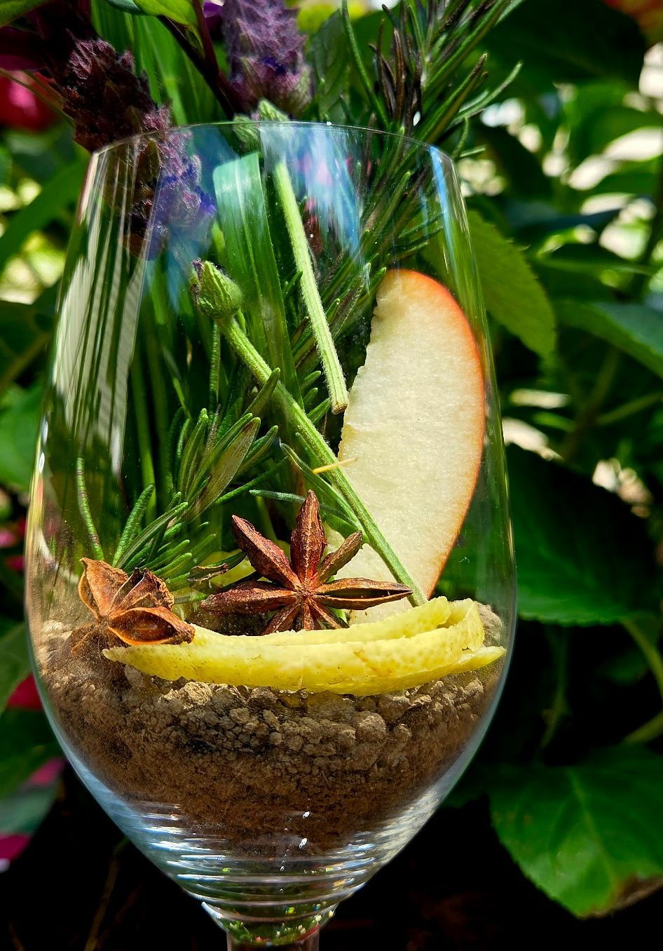 Clear wine glass with layered dessert, star anise, pear slice, and green foliage background