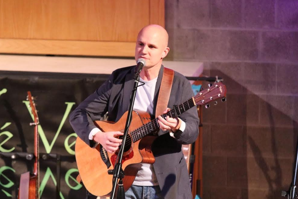 Musician playing acoustic guitar and singing on stage with a microphone