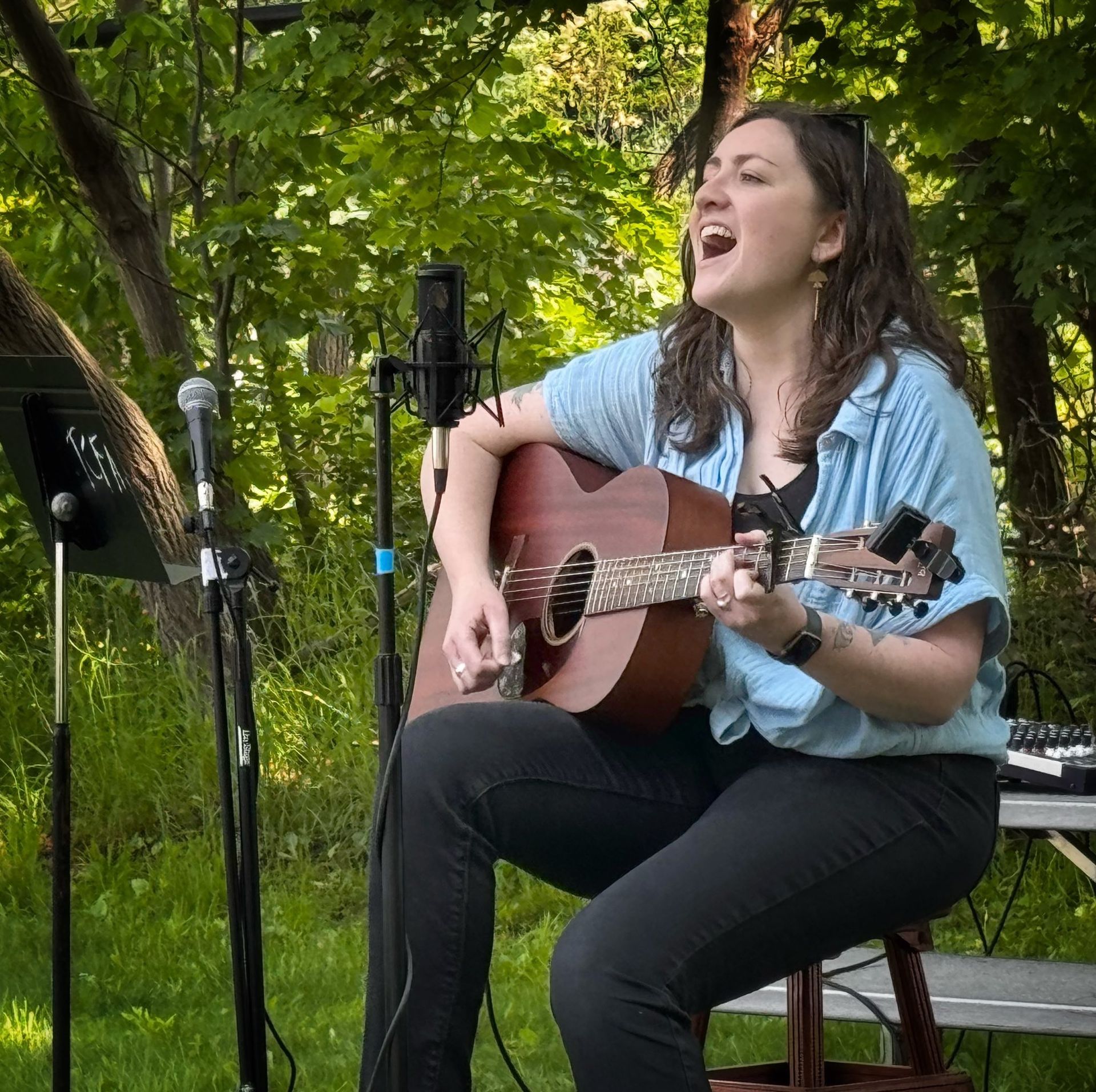 Woman singing and playing acoustic guitar outdoors on a green patio