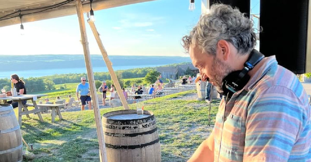Person under a canopy at an outdoor overlook, looking down near wooden barrels with a scenic valley in the background