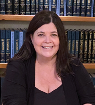 A woman is smiling in front of a bookshelf full of books