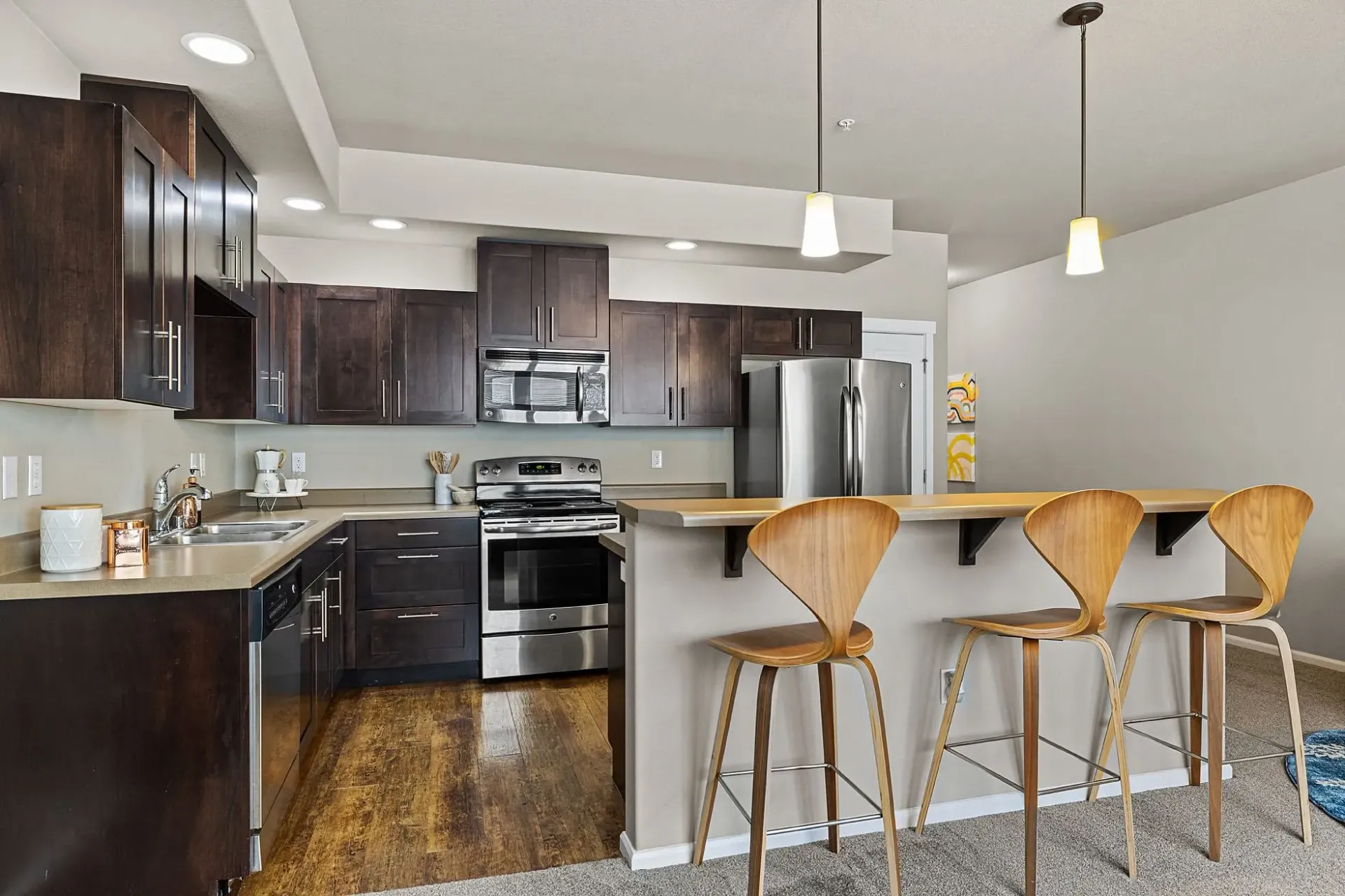 Modern kitchen with dark wood cabinets, stainless steel appliances, and a breakfast bar with wooden stools.
