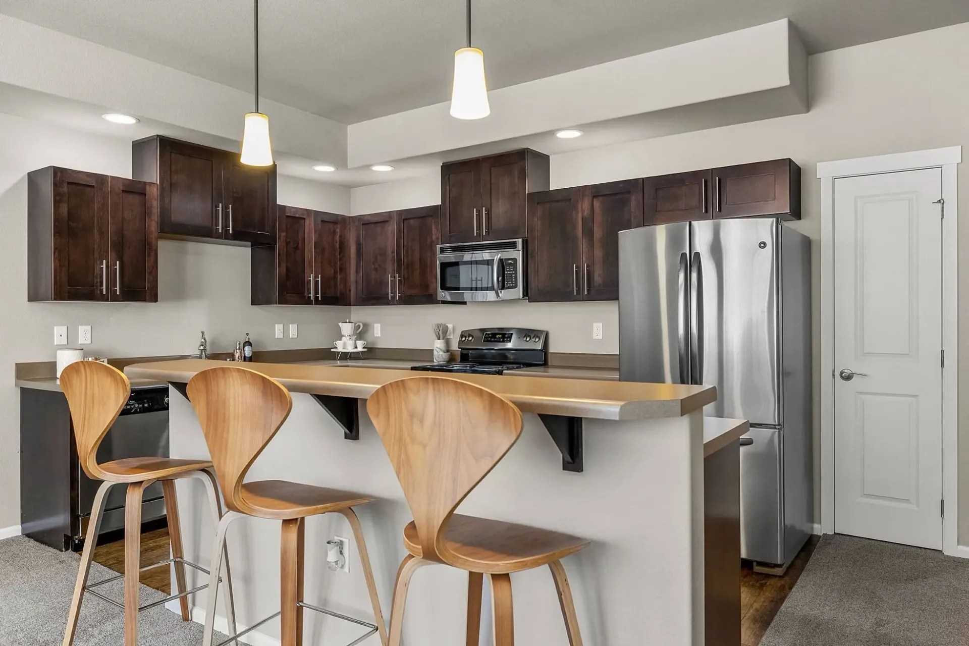 Modern kitchen with dark wood cabinets, stainless steel appliances, and a breakfast bar with three stools.