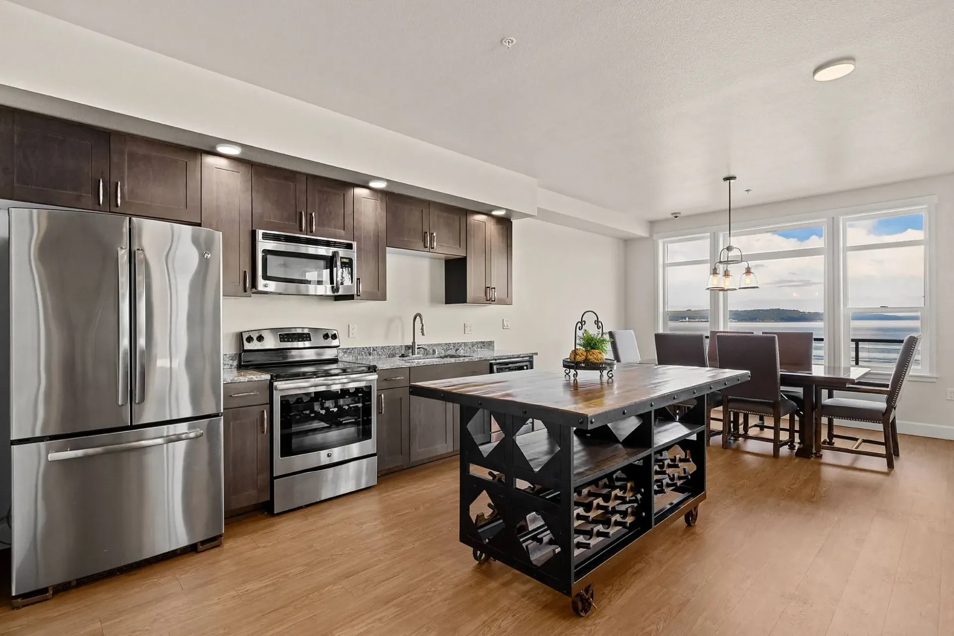 Modern kitchen with stainless steel appliances, an island with wine storage, and a dining area with a view.