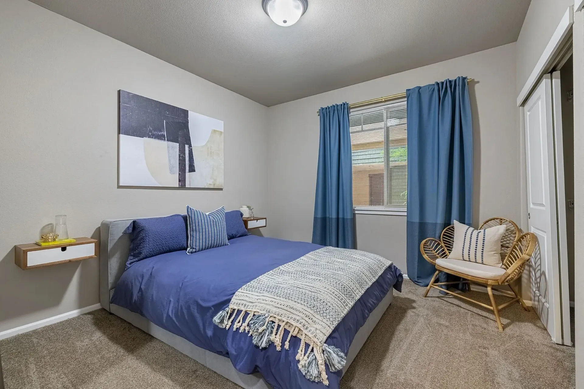 Bedroom with a queen-size bed, blue bedding, and a rattan chair.