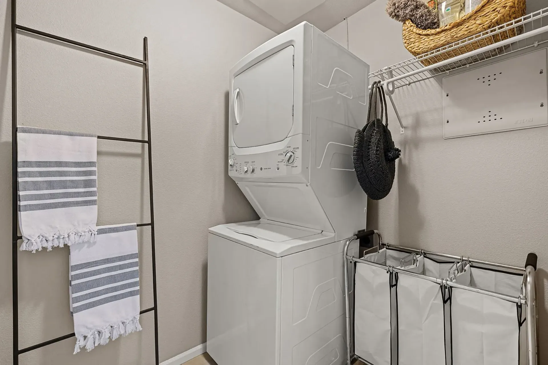 Stacked washer and dryer with a laundry hamper and decorative towels.