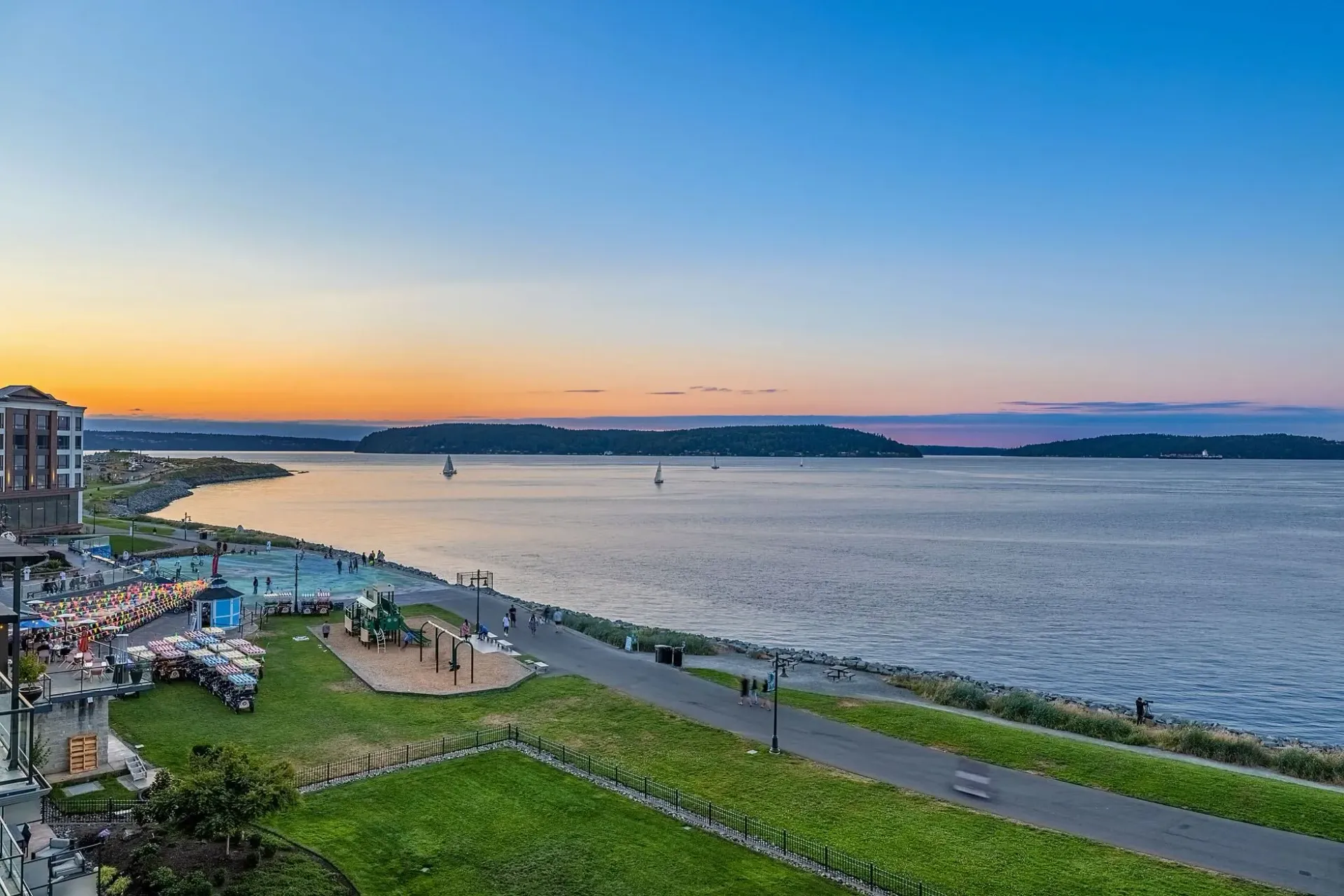 Waterfront community park with playground and walking path during sunset.