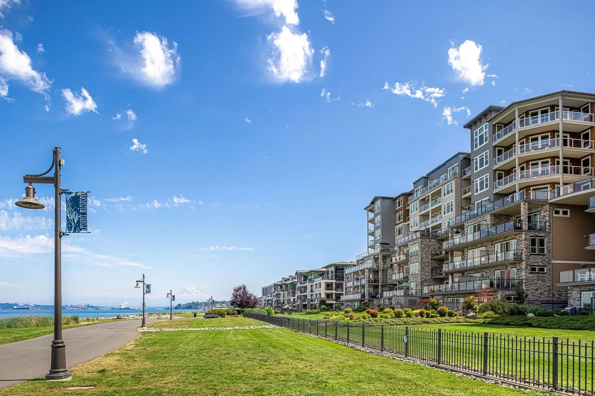 Apartment building exterior with balconies overlooking a park and water.