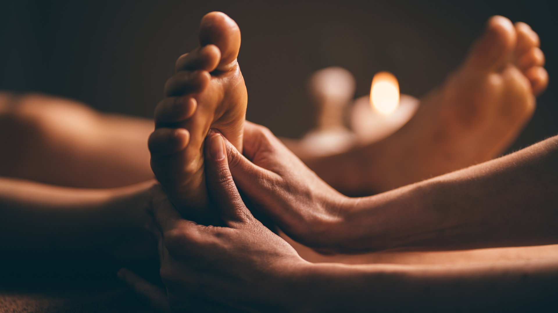 A person is getting a foot massage with a candle in the background.