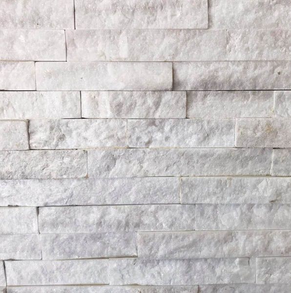 Primer plano de una pared de piedra blanca apilada con azulejos rectangulares texturizados.
