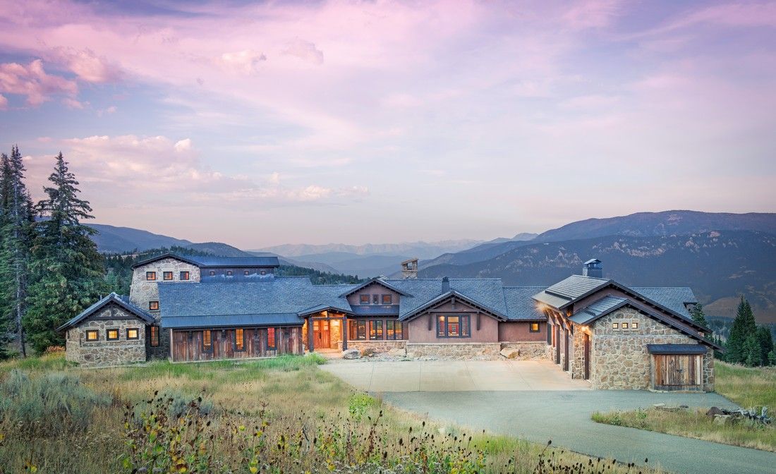 A large house is sitting on top of a hill with mountains in the background.