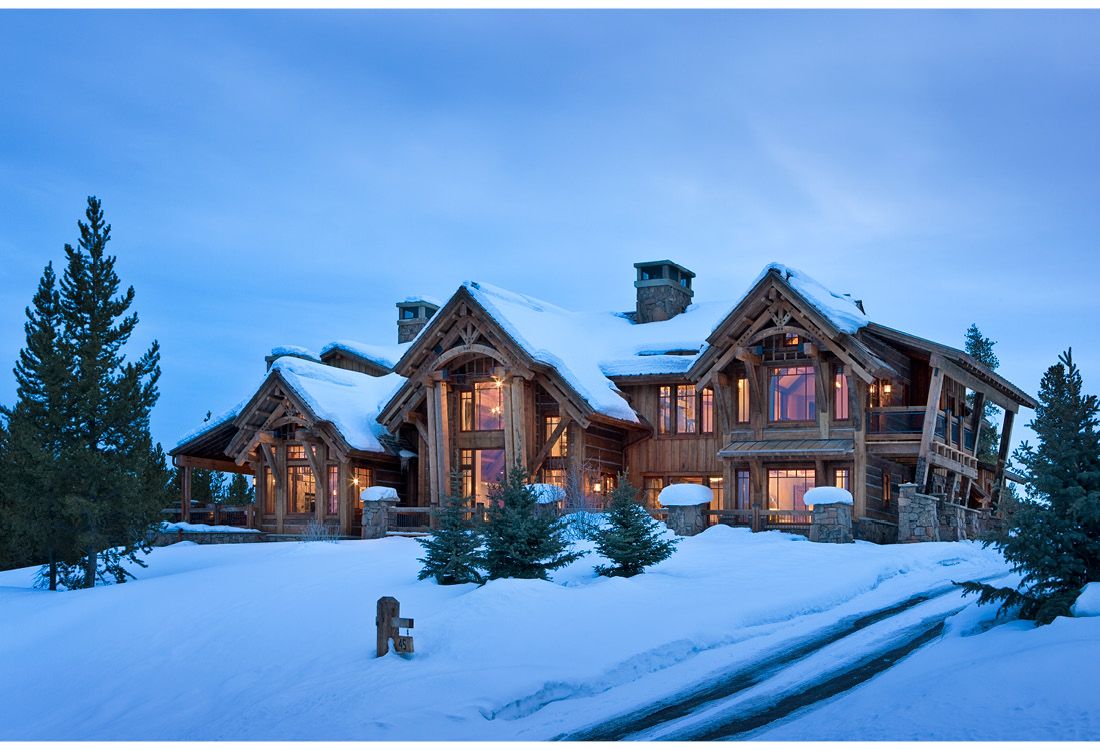 A large log cabin is surrounded by snow and trees