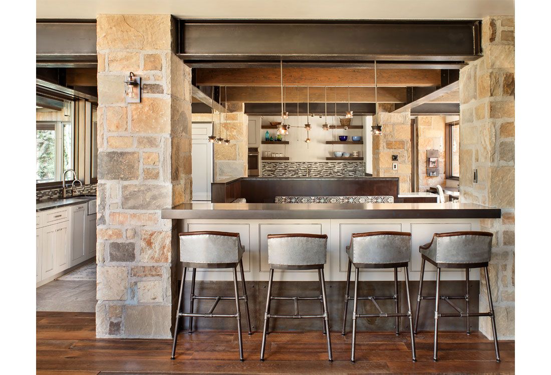 A kitchen with a bar and stools and a stone wall.