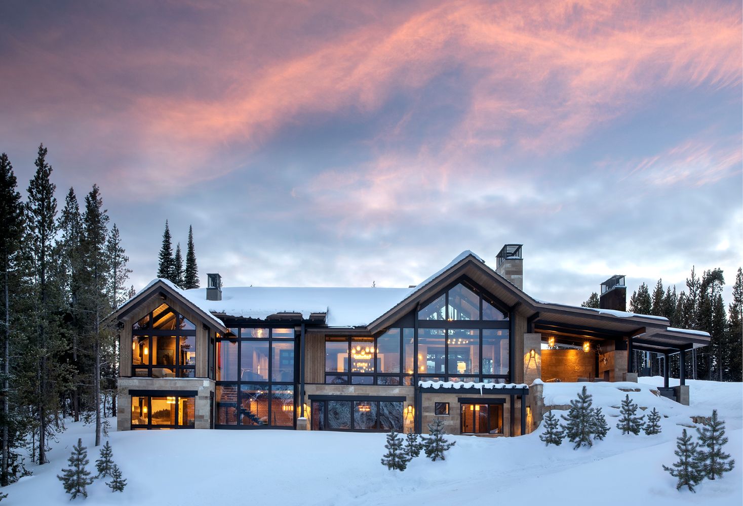 A large house with a lot of windows is surrounded by snow and trees.