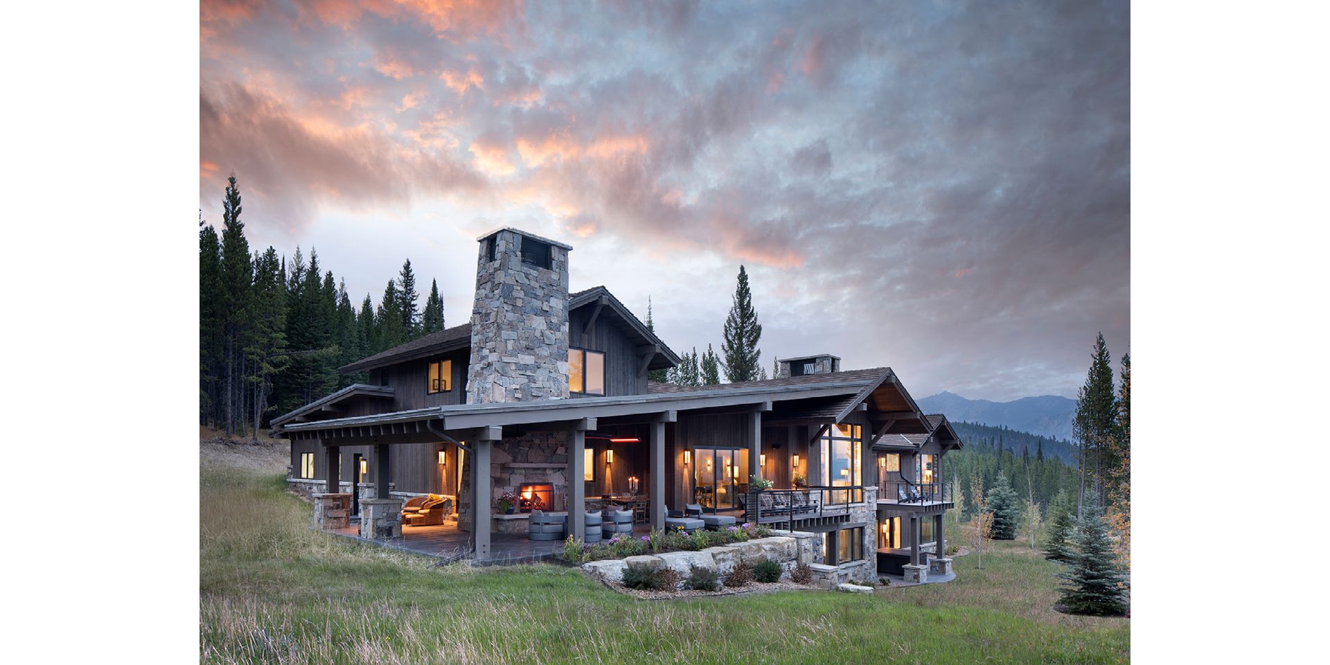 A large house is sitting on top of a grassy hill in the middle of a forest.