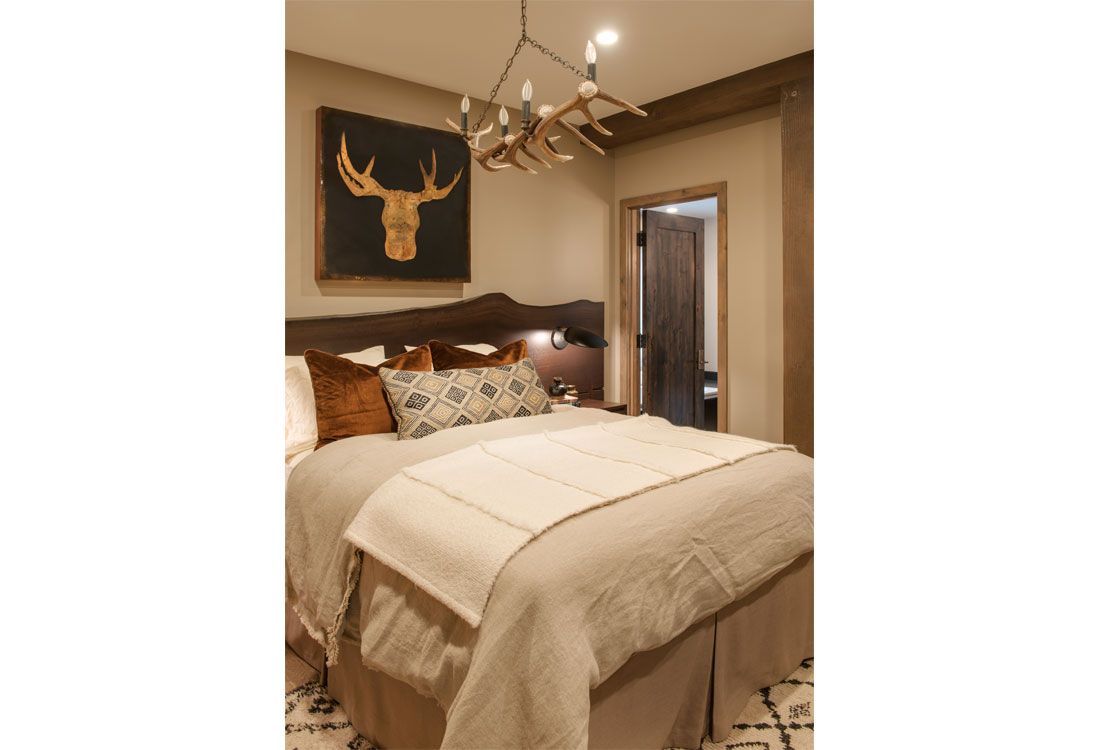 A bedroom with a bed , a chandelier , and a deer head on the wall.
