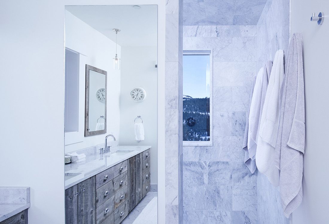 A bathroom with a walk in shower , sink , mirror and towels hanging on the wall.