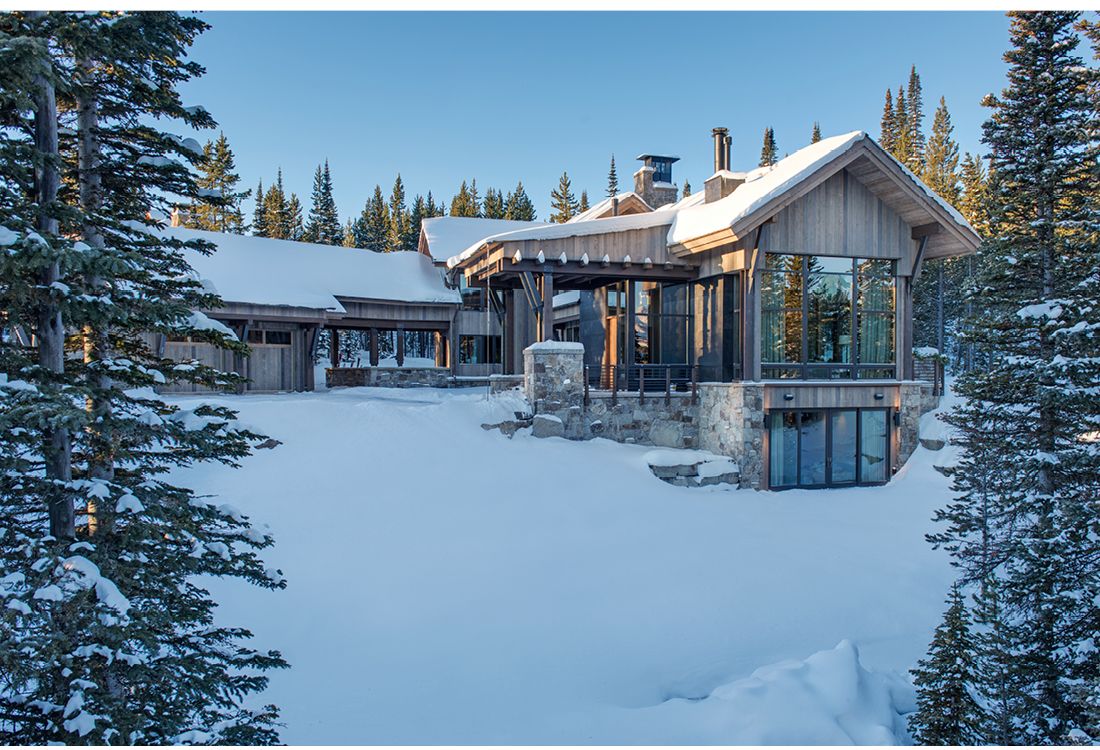 A large house is surrounded by snow covered trees in the mountains.