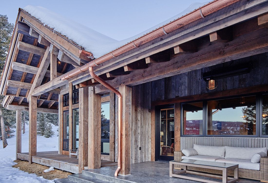 A wooden house with a copper gutter and a couch on the porch.