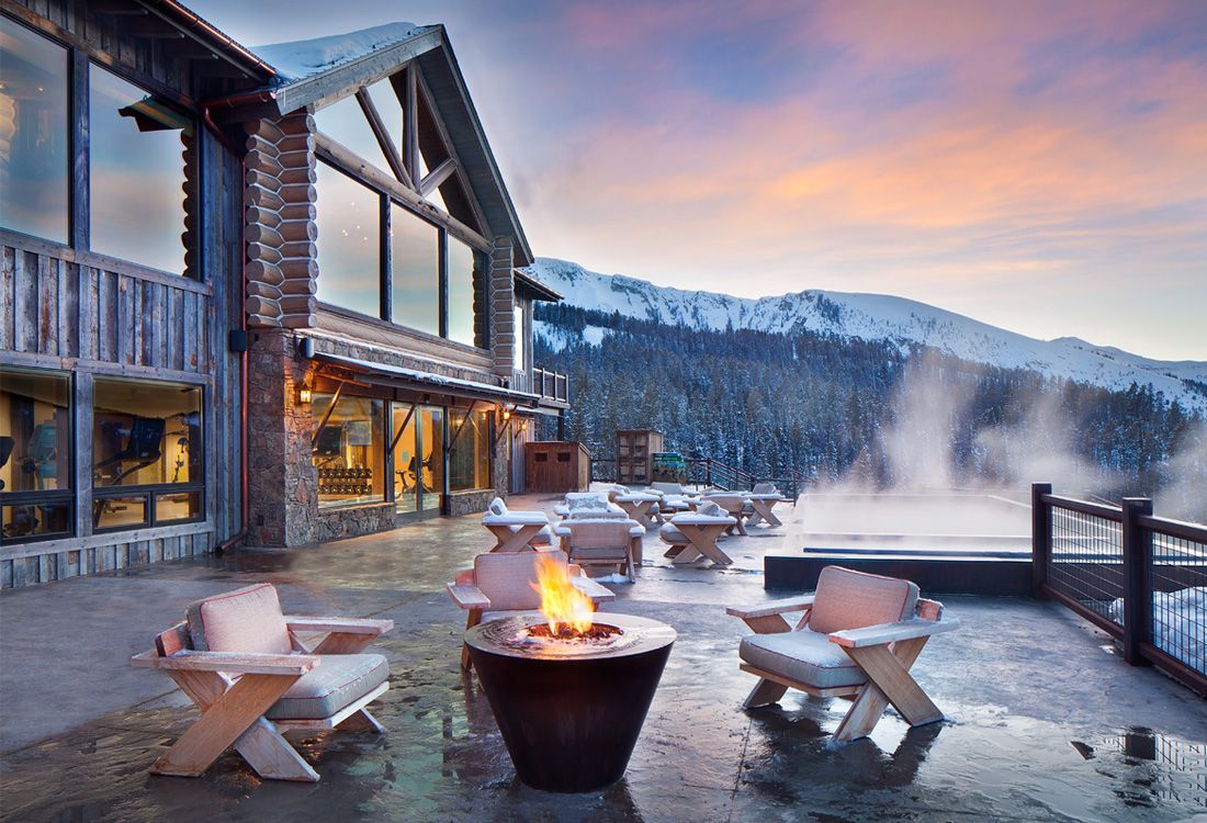 A patio with chairs and a fire pit in front of a house with mountains in the background.