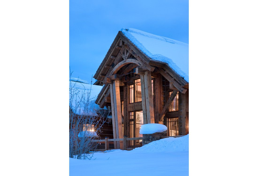 A wooden house covered in snow with a blue sky in the background.
