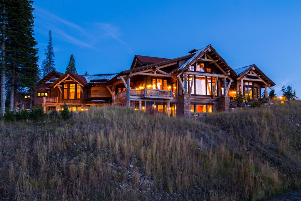 A large log cabin is sitting on top of a grassy hill at night.