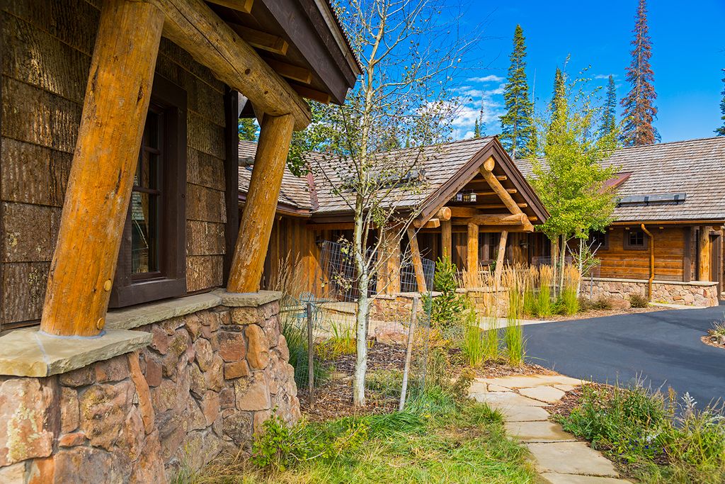 A log cabin with a stone wall and a wooden roof is surrounded by trees and grass.