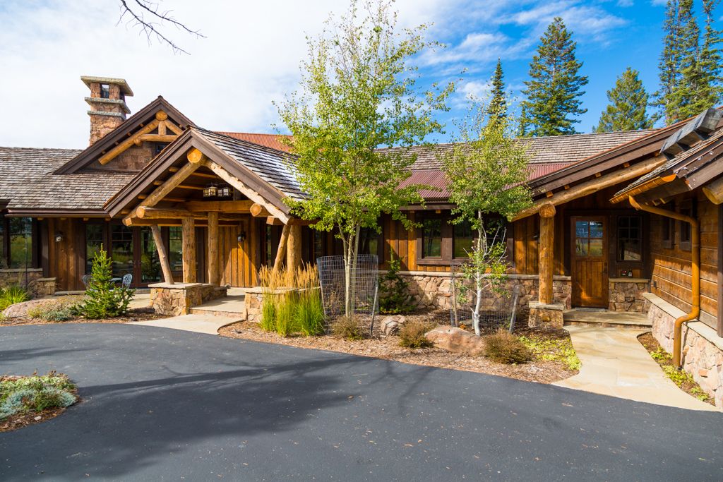 A large wooden house with a driveway and trees in front of it.