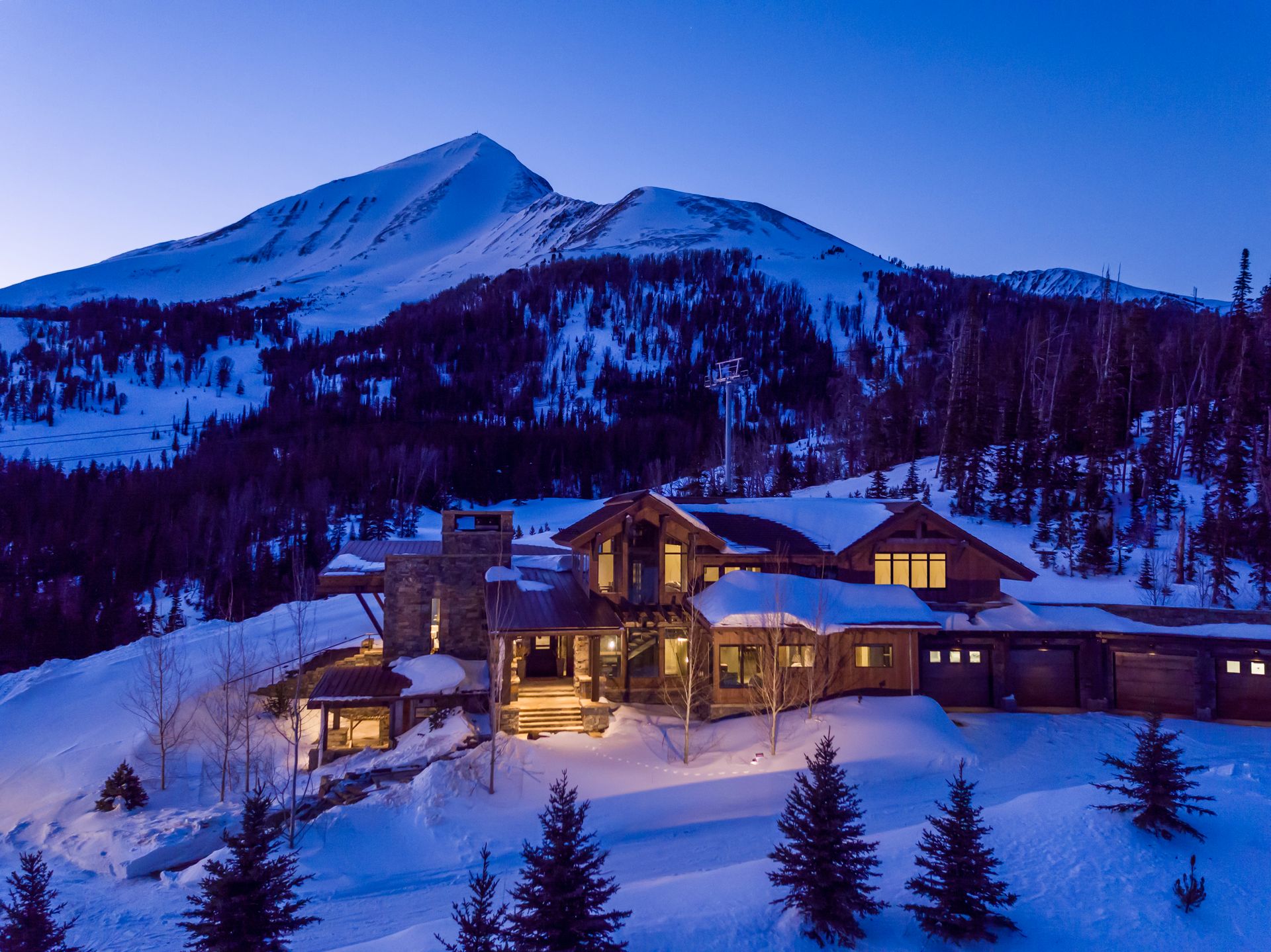 An aerial view of a house in the snow with a mountain in the background.