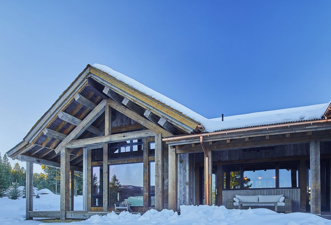 A large wooden house covered in snow with a blue sky in the background.