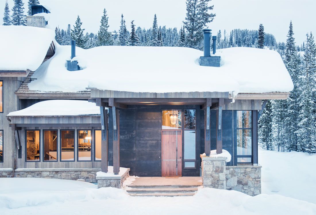 A house is covered in snow in the middle of a snowy forest.