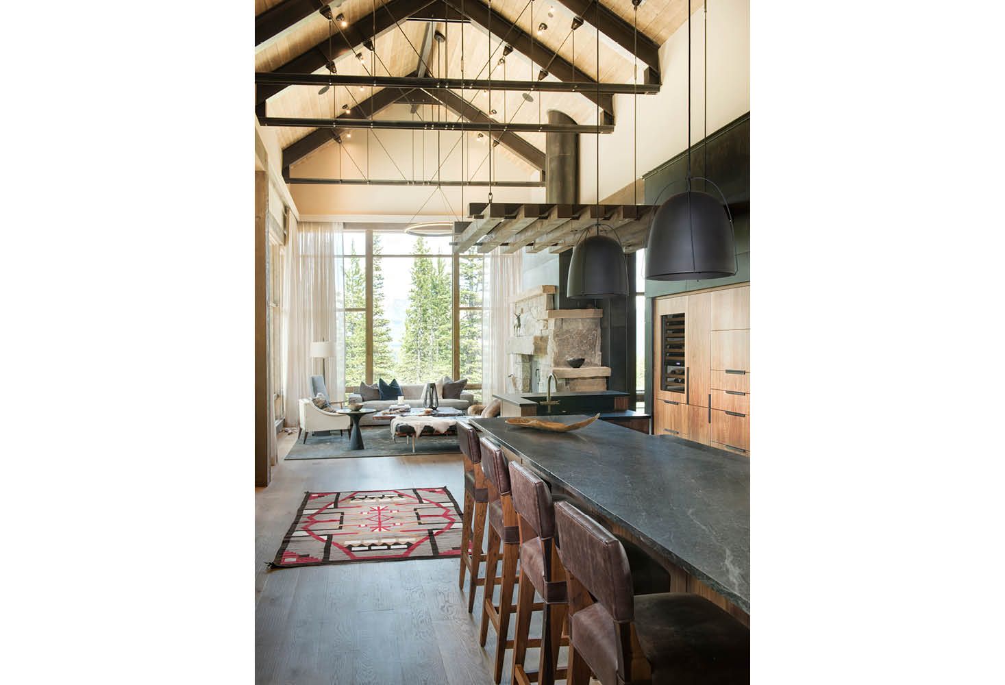 A kitchen with a long counter and stools in a house with a vaulted ceiling.
