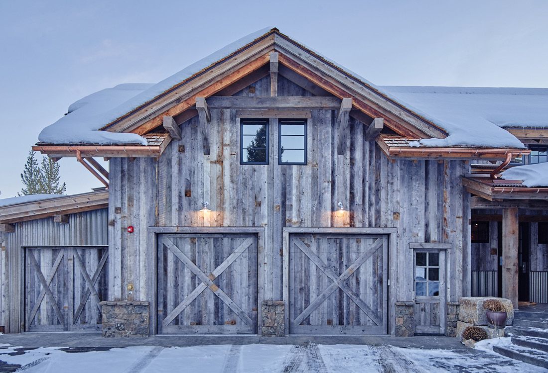 A large wooden barn with two garage doors is covered in snow.