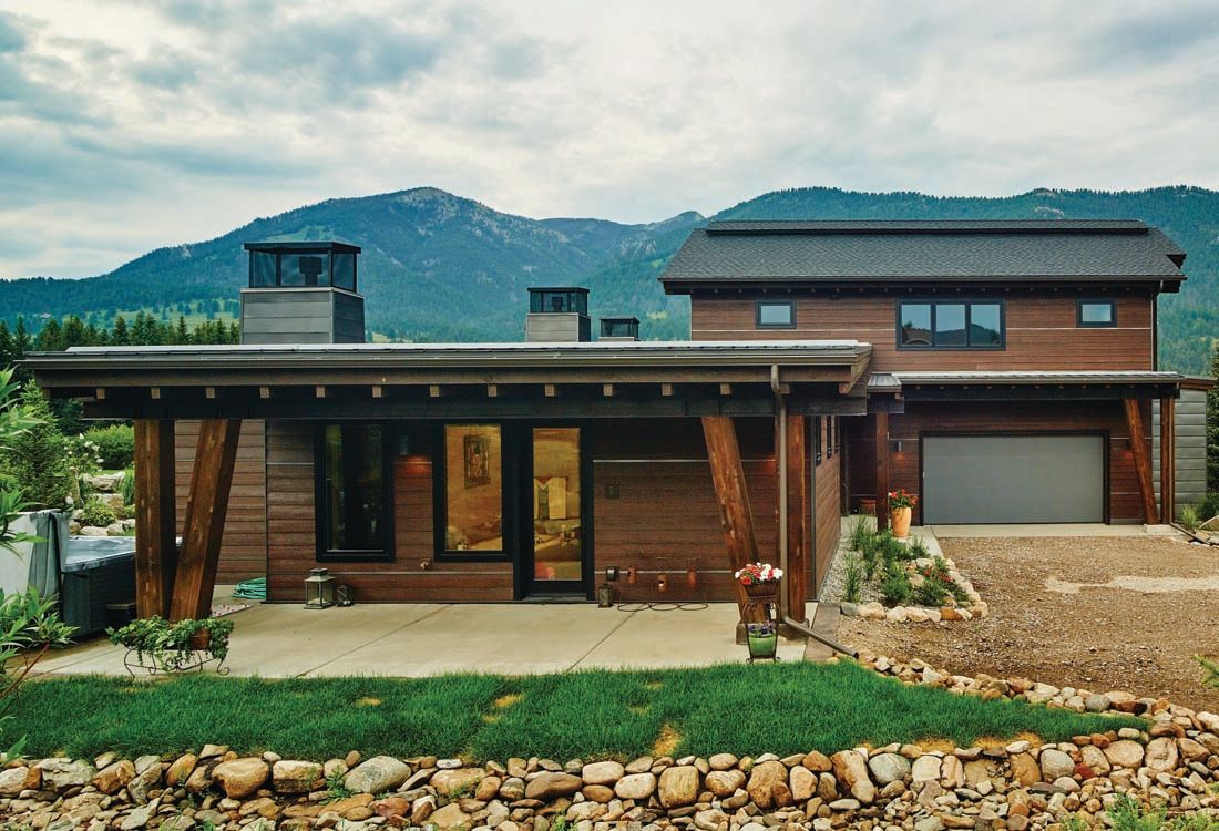 A house with mountains in the background and a stone wall in front of it