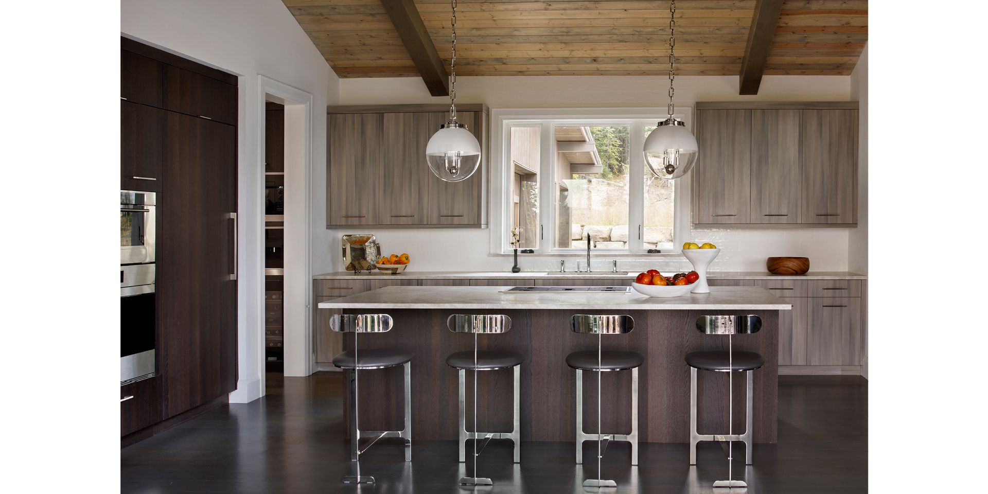 A kitchen with a large island and stools and a wooden ceiling.