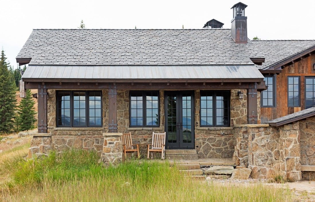 A small stone house with a metal roof is sitting in the middle of a grassy field.