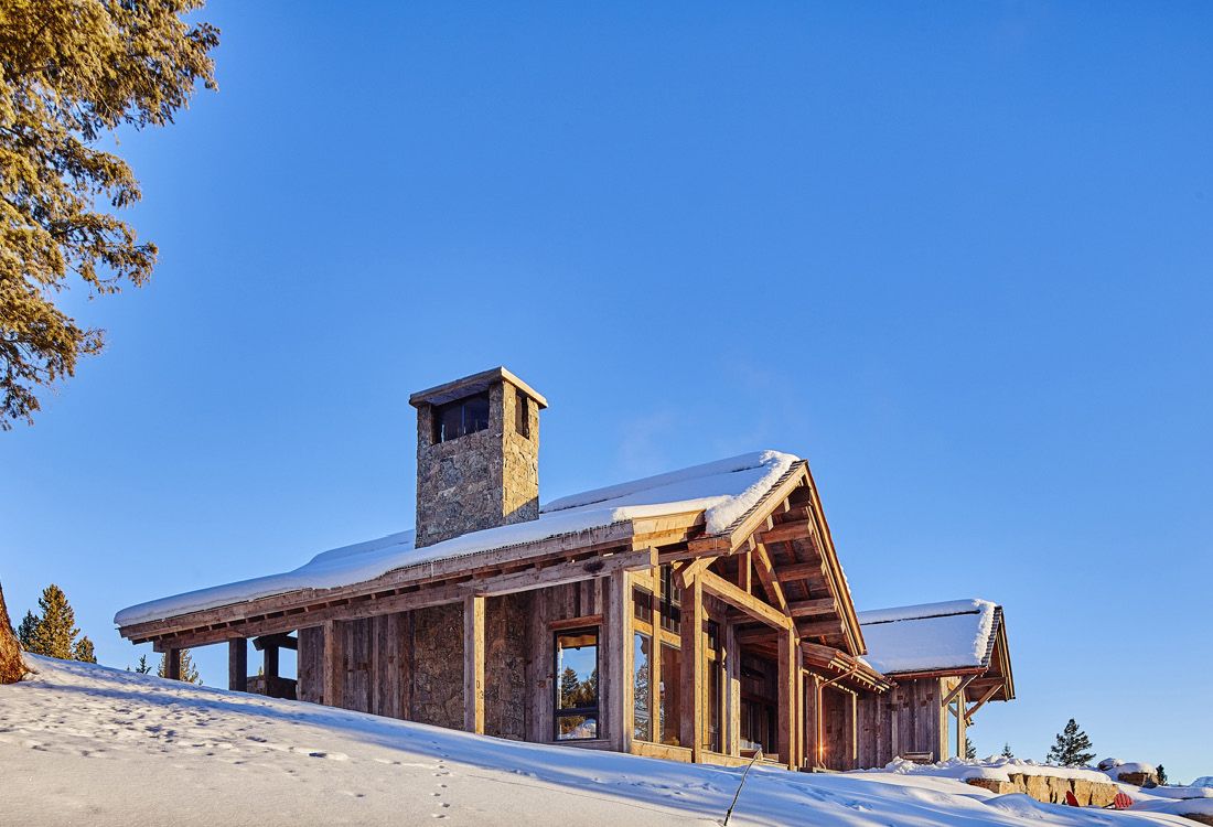 A large wooden house is sitting on top of a snow covered hill.