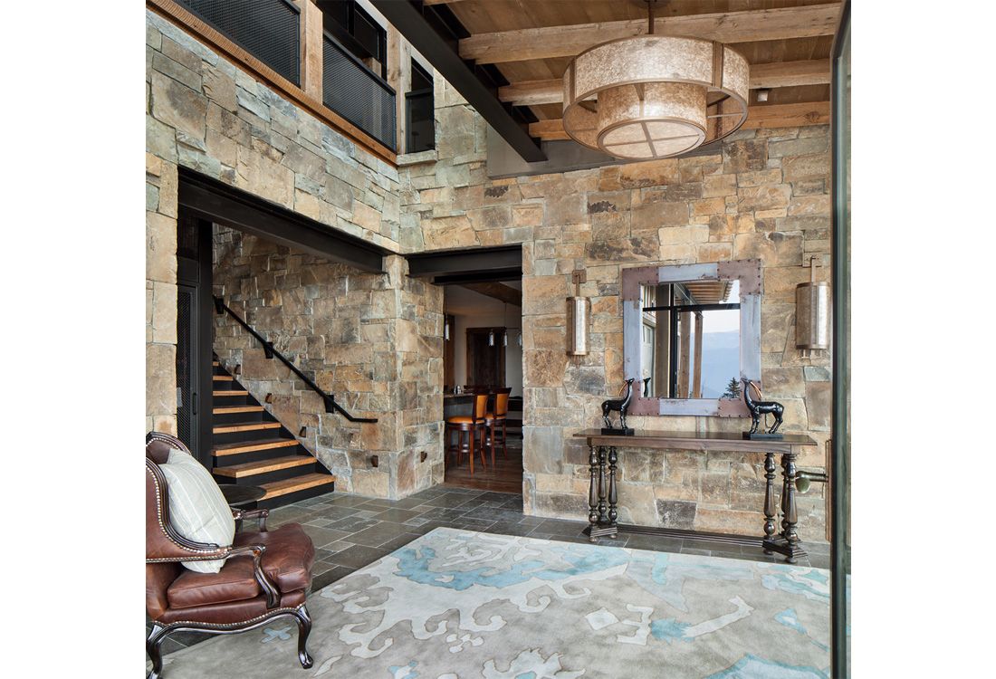 A living room with a chair , table , mirror and stairs.