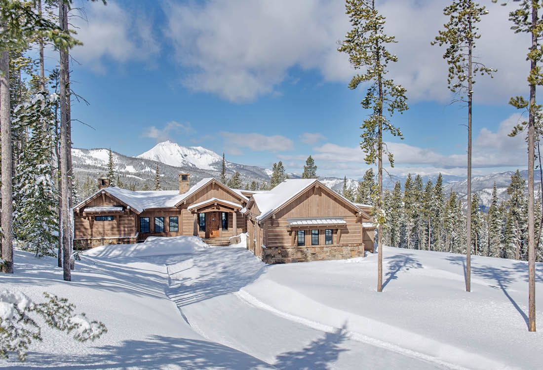A house in the middle of a snowy forest with mountains in the background.