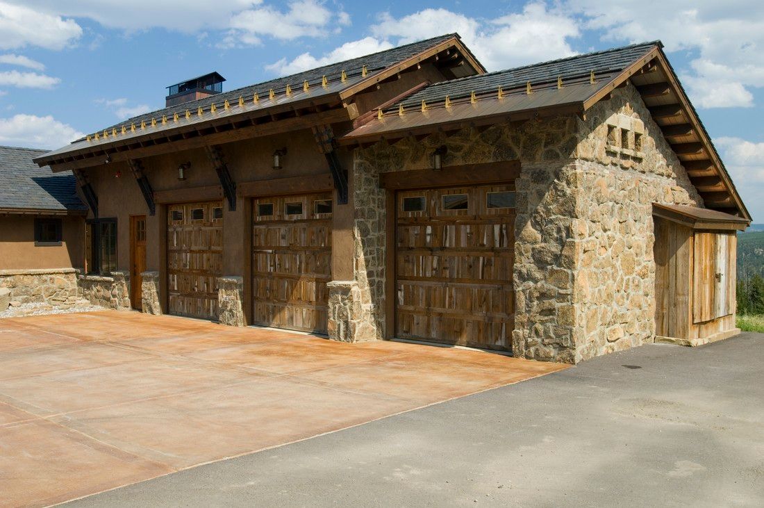 A large stone house with three garage doors and a driveway.