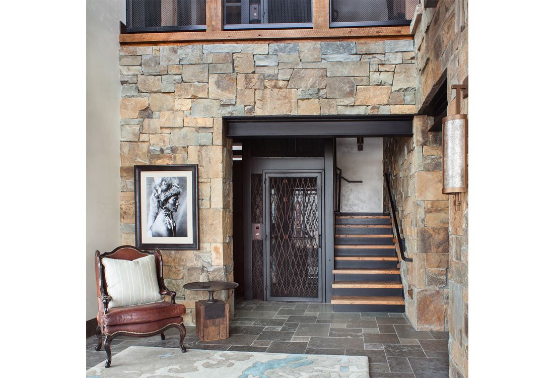 A living room with a chair , stairs and a stone wall.
