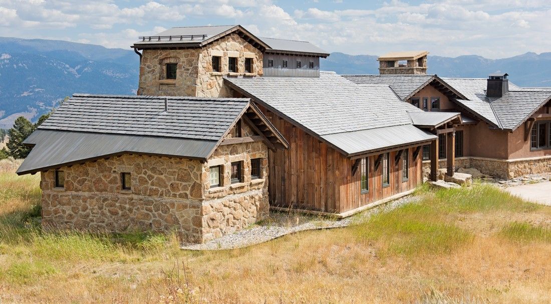 A large stone house with a slate roof is sitting on top of a grassy hill.