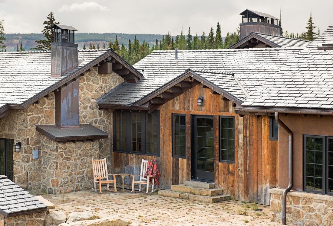 A large stone house with a slate roof and rocking chairs in front of it.