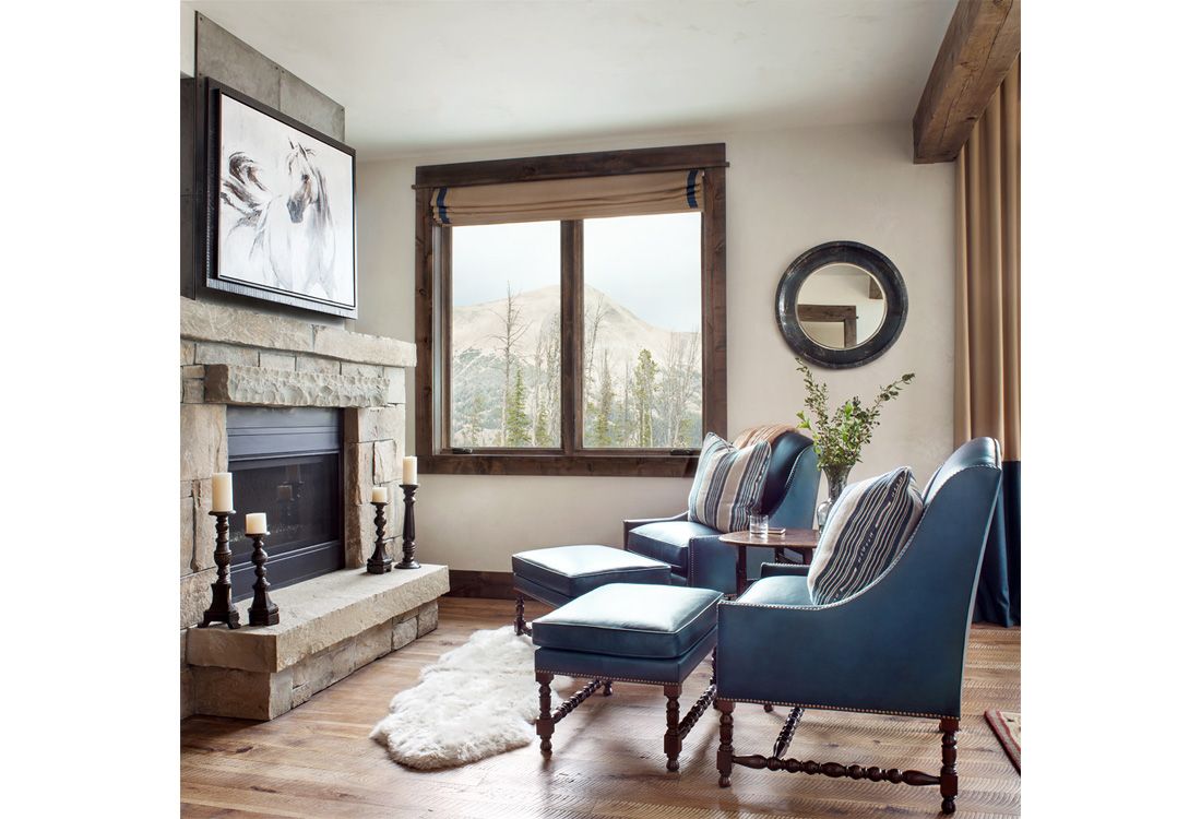 A living room with a fireplace , chairs , ottomans and a television.